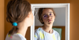 Mädchen schaut sich kritisch im Spiegel an